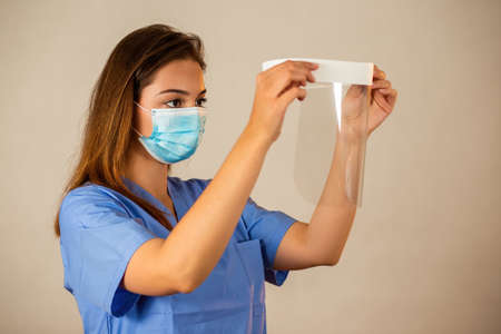 Woman attaching face shield in a hospital from side view. Young Caucasian nurse wearing surgical...