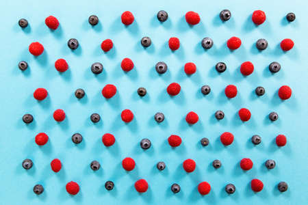 Fresh raspberries and blueberries alternately arranged on blue background. Little colorful berries organized on turquoise paper. Color table full of small heatlhy sweet fruit.の写真素材
