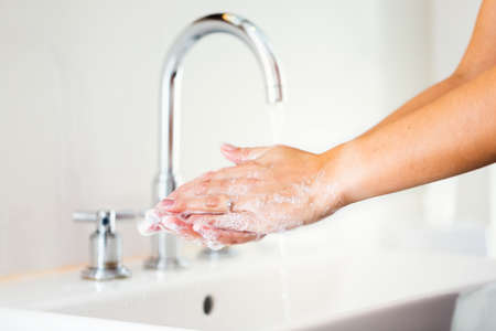 Woman washing hands with soap in bathroom with flowing water. Female cleaning under running water as...