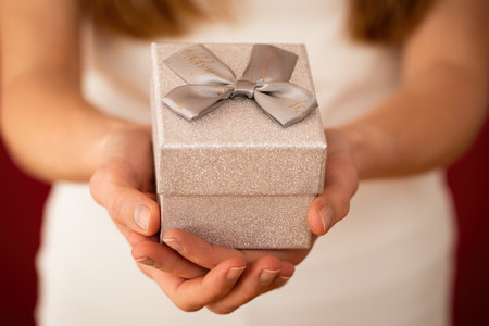 Blurred female holding silver gift in hands on red background. Woman with little present with ribbon...