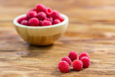 Heap of raspberries lying on a wooden board in kitchen prepared to be served. Fresh ripe fruit of...