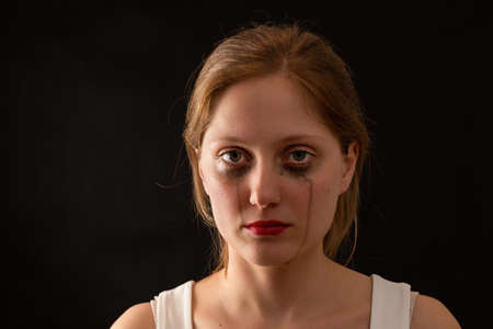 Blonde female with sad expression from front on black background. Young woman crying with blank look in darkenss. Upset female without smile in depression.の写真素材