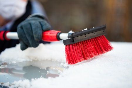 Man in gloves removing snow from a roof of a car with red brushの写真素材