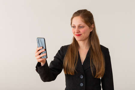 Businesswoman holding a phone in hear hand and looking into it in her officeの写真素材