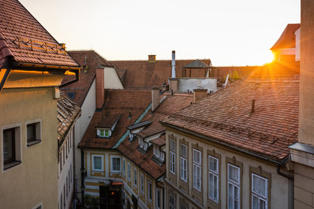 Sun setting over rooftops with red tiles in a city with old housesの写真素材