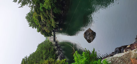 A quiet waterway embraced by forests on both sides. A small boat in the center completes the serene atmosphere.の写真素材