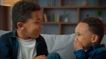 Two little boys friendly talking laughing at home. Ethnic African American multiracial multiethnic male kids schoolboys pupils sons indoors talk laugh together. Children brothers friends conversationの写真素材