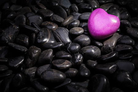 An illuminated pink heart lying on black stonesの写真素材
