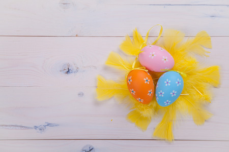 Painted eggs and yellow feathers lying on a white wooden table
