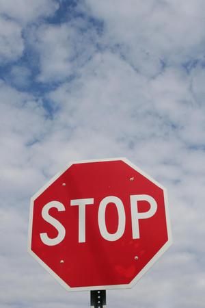 A bright red stop sign high in the blue sky with white clouds surrounding.の写真素材