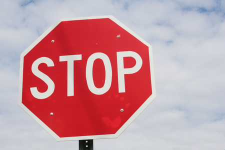 A bright red stop sign high in the blue sky with white clouds surrounding.の写真素材