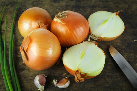 Whole and sliced onions on wooden cutting boardの写真素材