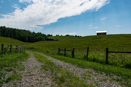 Country background of a gravel path leading into a fenced pasture with a Mail Pouch painted barn up on a hill to the right.のeditorial素材