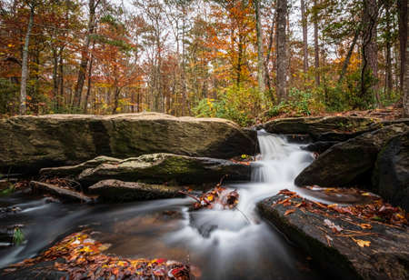 Long exposure shot of the beautiful Cheaha Falls with bright autumn color in the background.の写真素材