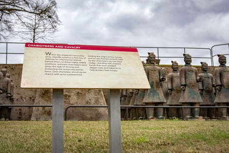 Troy, Alabama, USA-March 20, 2021: Informational sign in the foreground with charioteers and cavalry terracotta warriors out of focus in the background at the Janice Hawkins Cultural Arts Park on the campus of Troy University.のeditorial素材