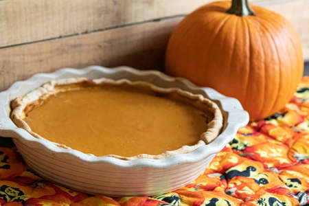 Homemade pumpkin pie on orange and yellow, Halloween-themed cloth with a small pumpkin in the background.の写真素材