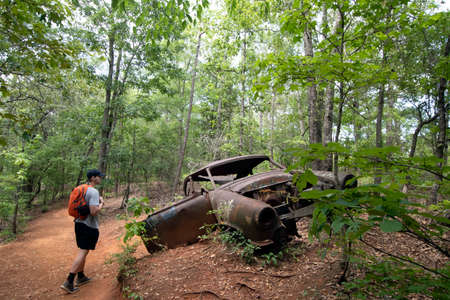 Lumpkin, Georgia, USA- June 6, 2021: Old abandoned car at the site of an old homestead with male hiker looking on at Providence Canyon State Park in southwest Georgia.のeditorial素材