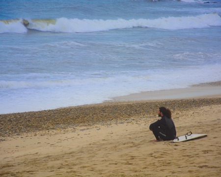 sitting surfer contemplating the ocean at noon, esposende, portugalの写真素材