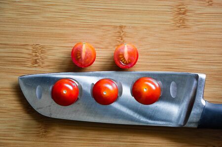 3 cherry tomatoes balancing on a kitchen knife over a wooden cutting board