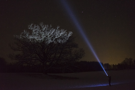 Man standing outdoors at night in Sweden Scandinavia winter landscape shining with flashlight at...