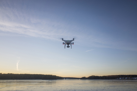 White drone flying in air over ice lake in Sweden Scandinavia Europe on cold winter evening. Nice...