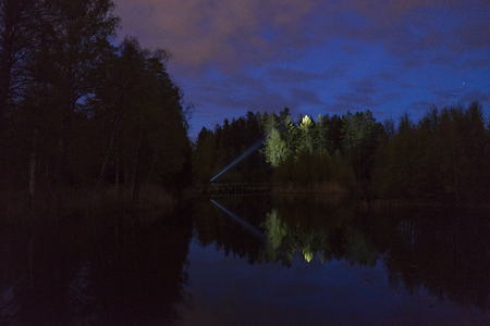 Man standing outdoor at dark night shining with flashlight. Mystical and abstract photo of Swedish nature and landscape.の写真素材