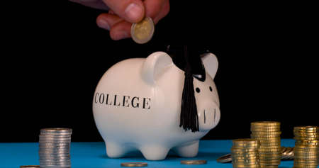 Budget for College. Student Throws Coins Into Piggy Bank for College Taking Coins from His Budget.の写真素材
