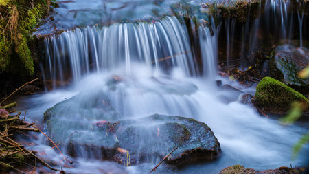Gentle waterfall cascading over mossy rocks in a serene forest setting during the early morning...