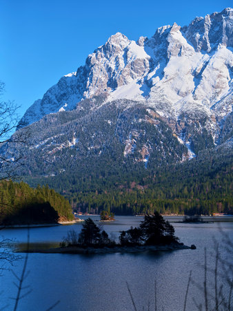 Majestic snow-capped mountains surround a tranquil lake under a clear blue sky in the afternoon