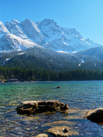 Mountain view over crystal clear lake with rocky shoreline and snow-capped peaks in bright sunlight