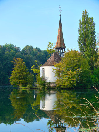 Charming lakeside chapel surrounded by trees on a clear day in a serene natural settingの写真素材