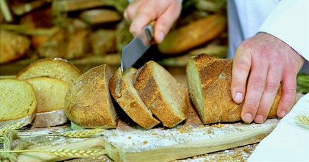 Detailed View Of Skilled Baker Slicing Sourdough Loaf With Flour Dusting And Warm Lighting