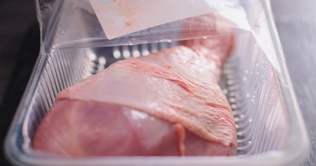 Raw chicken leg in a plastic container ready for cooking at a kitchen countertop during late afternoonの写真素材