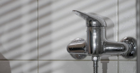 Water faucet with light and shadow patterns in a bathroom setting during the day