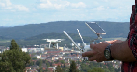 Person operates a drone above a city in the daytime with hills in the background