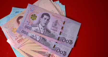 Thai banknotes spread on a table with red background showing different denominations and colors...