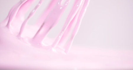 Mixing pink batter in a bowl with a whisk for baking during a sunny afternoon in a kitchenの写真素材