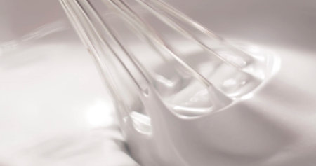 Whisk mixes egg whites in a clear bowl during a baking session in a kitchen on a sunny afternoon