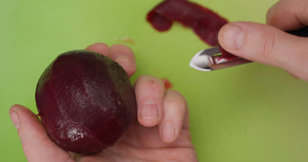 Peeling beetroot in a kitchen on a green cutting board in the afternoon with a simple knife