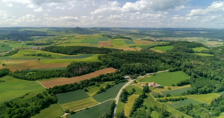 Green fields and hills stretch across the countryside with a winding road and small houses below in...