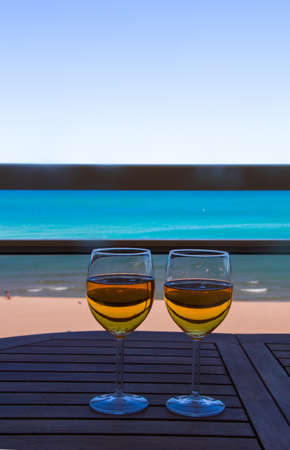 two glasses full of cider on top of a table with the sea in the backgroundの写真素材