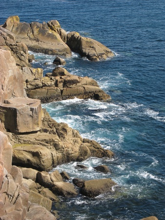 Big brown granite rocks at the coast, with dark blue sea の写真素材
