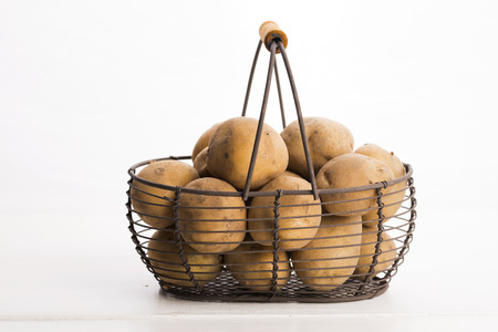 uncooked potatoes in wire basketの写真素材