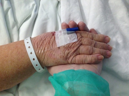 Two hands clasping on hospital bedの素材