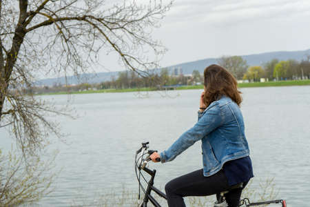 Young woman standing on her bike by the lake.