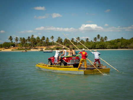 Small car buggy crossing the river in a primitive boat with men pushing bamboo in Ceara, Brazilのeditorial素材