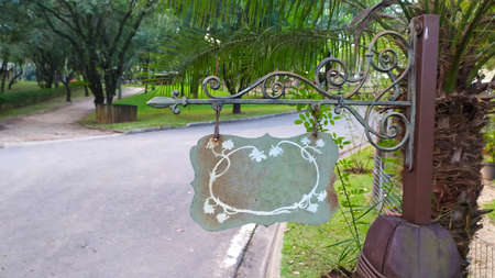 Capable of advertising on a iron stand hanging on a wooden post in tropical landcape with a road in backgroundの写真素材
