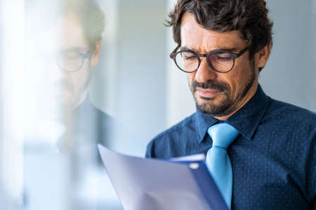 Business man wearing glasses holding paper document folder. Successful male portrait reading...