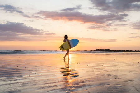 Surfer girl silhouette. Surf woman walking with surfboard on the beach. golden hour beautiful colorsの写真素材
