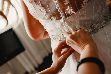 Bride getting ready, they help her by buttoning the buttons on the back of her dress.